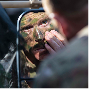 soldier applying camoflauge facepaint in mirror.